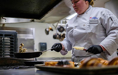 Culinary student cooking a dish in the college kitchen.