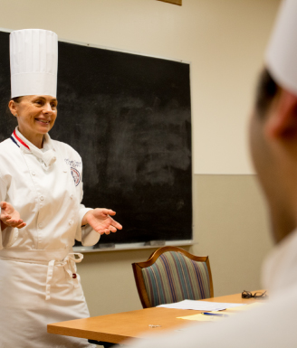 Chef educator speaking to students in front of a chalkboard