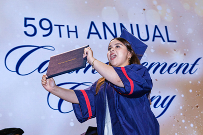 Student raising their diploma in the air on stage.