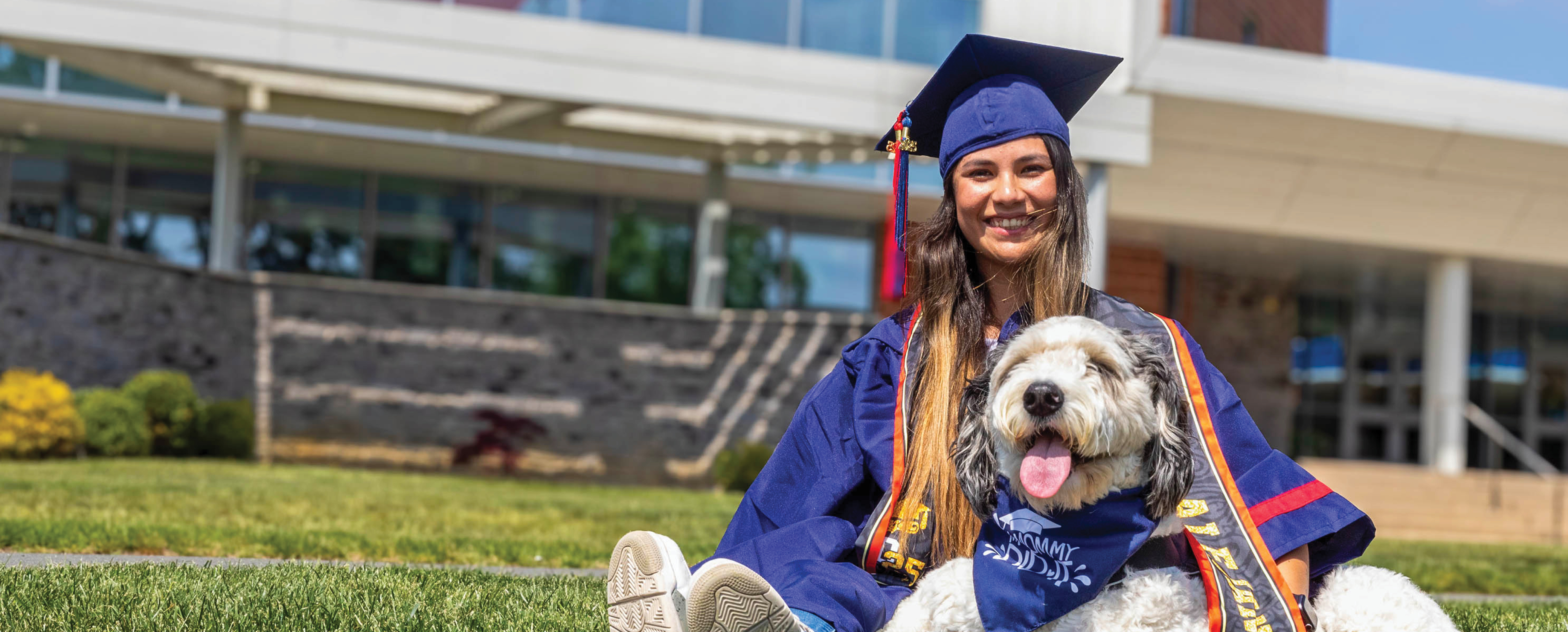 Graduate and her dog on the grass at Mays Landing campus.