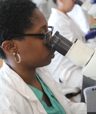 female student using microscope in a lab coat
