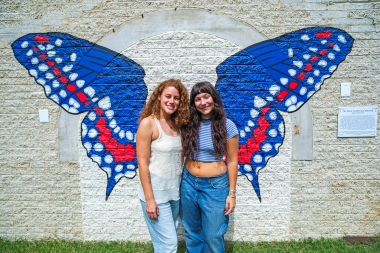 Cristina Lopez and Delaney Cluff stand in front of butterfly mural they helped paint