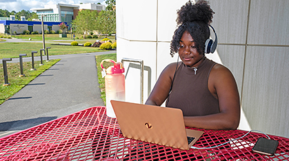 Atlantic Cape student works on a laptop at an outdoor table on campus.