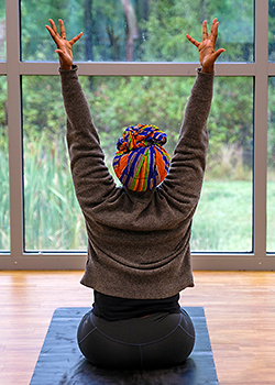 A woman practicing yoga in a studio, looking out a window toward a forested landscape.